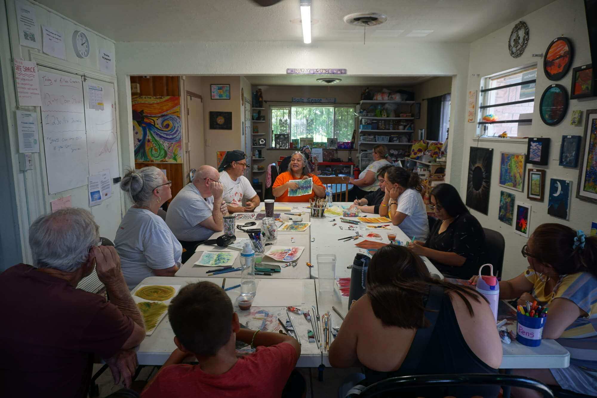 Woman in orange shirt showing off artwork to group around a table